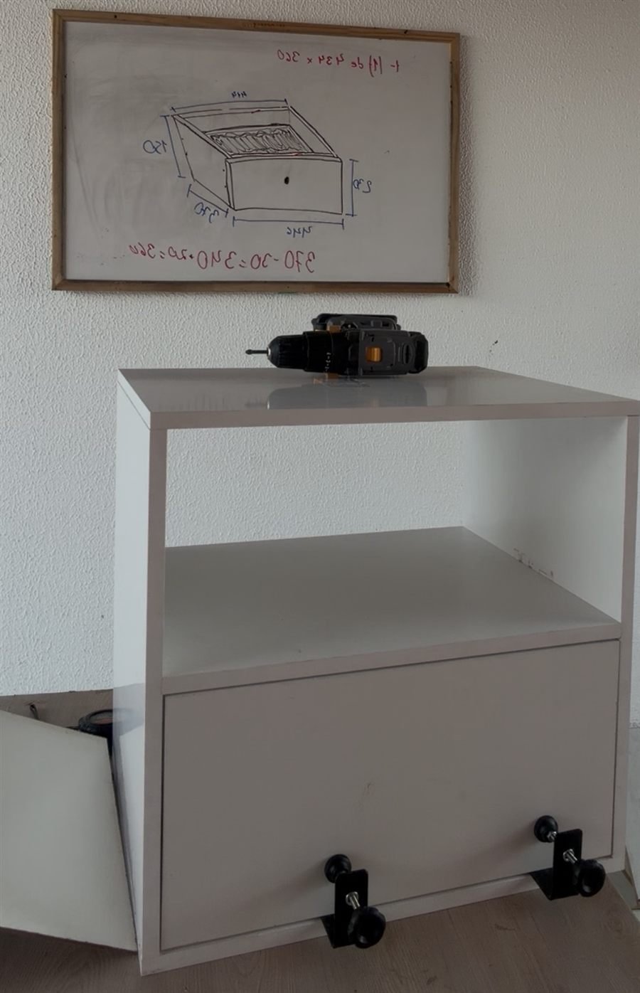 Mesa de cabeceira branca montada, diante do quadro com as medidas da gaveta